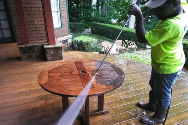Technician pressure washing a wood deck, with the cleaned boards showing their natural color